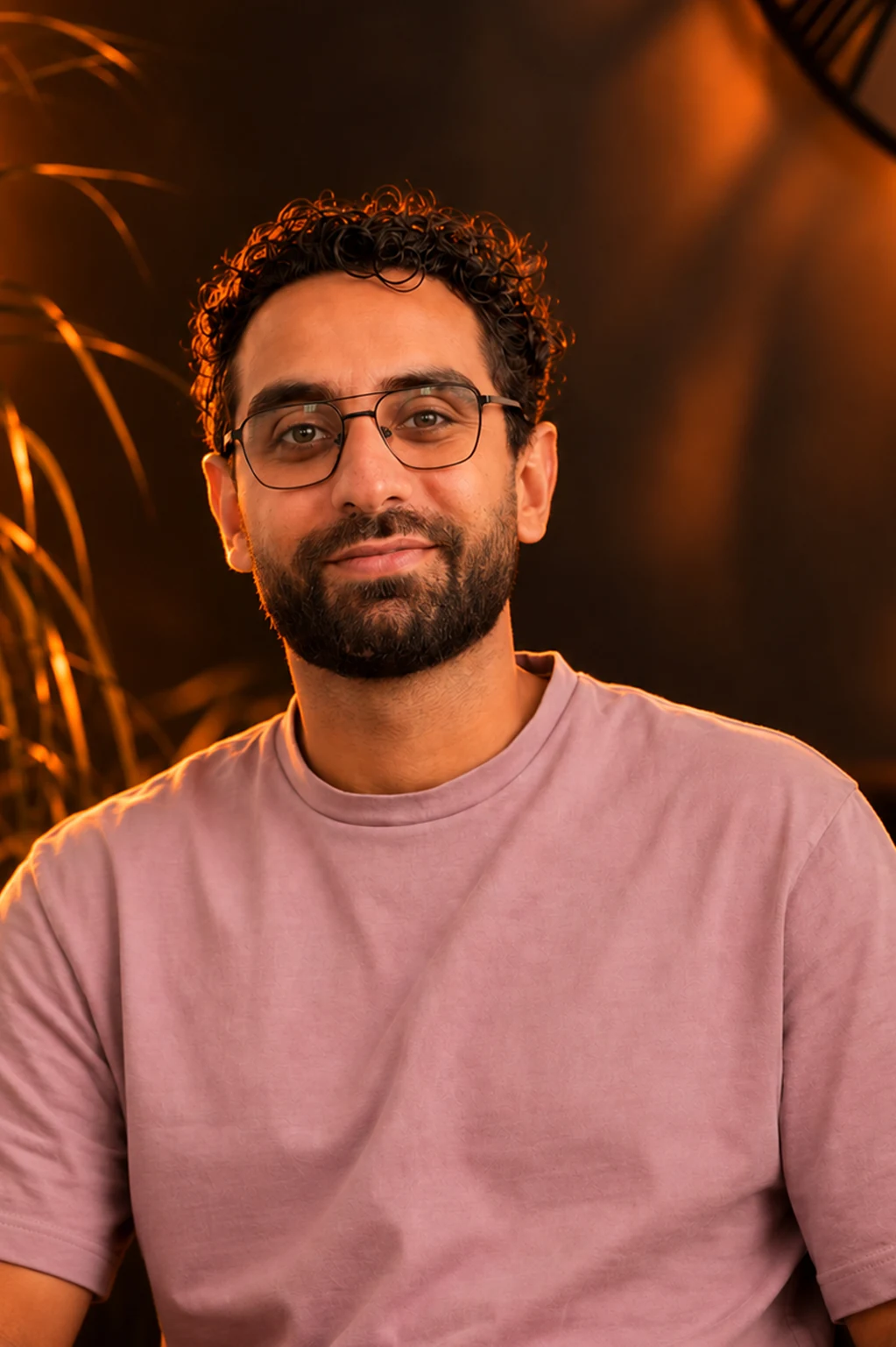 Hussein Deeb, portrait: dark studio, warm rim light, patterned rust and cream shirt, looking straight at the camera.